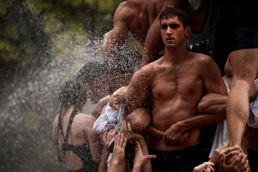 Young men and women link arms at the base of a monument to help others climb it.