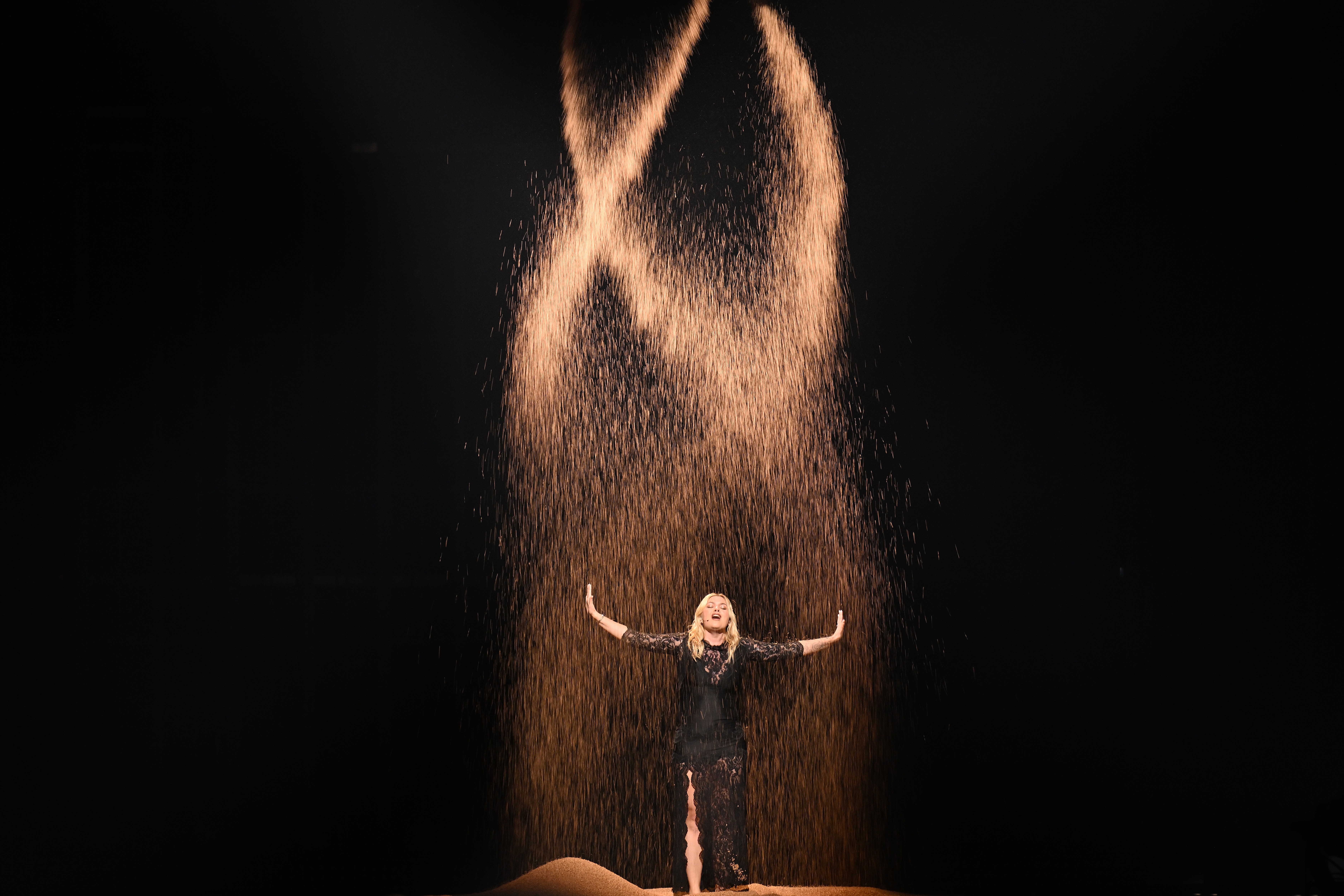 The performer sings when her sand-like particles fall around her.