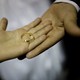 A small hand holding a gold wedding band rests on top of another person's larger hand.