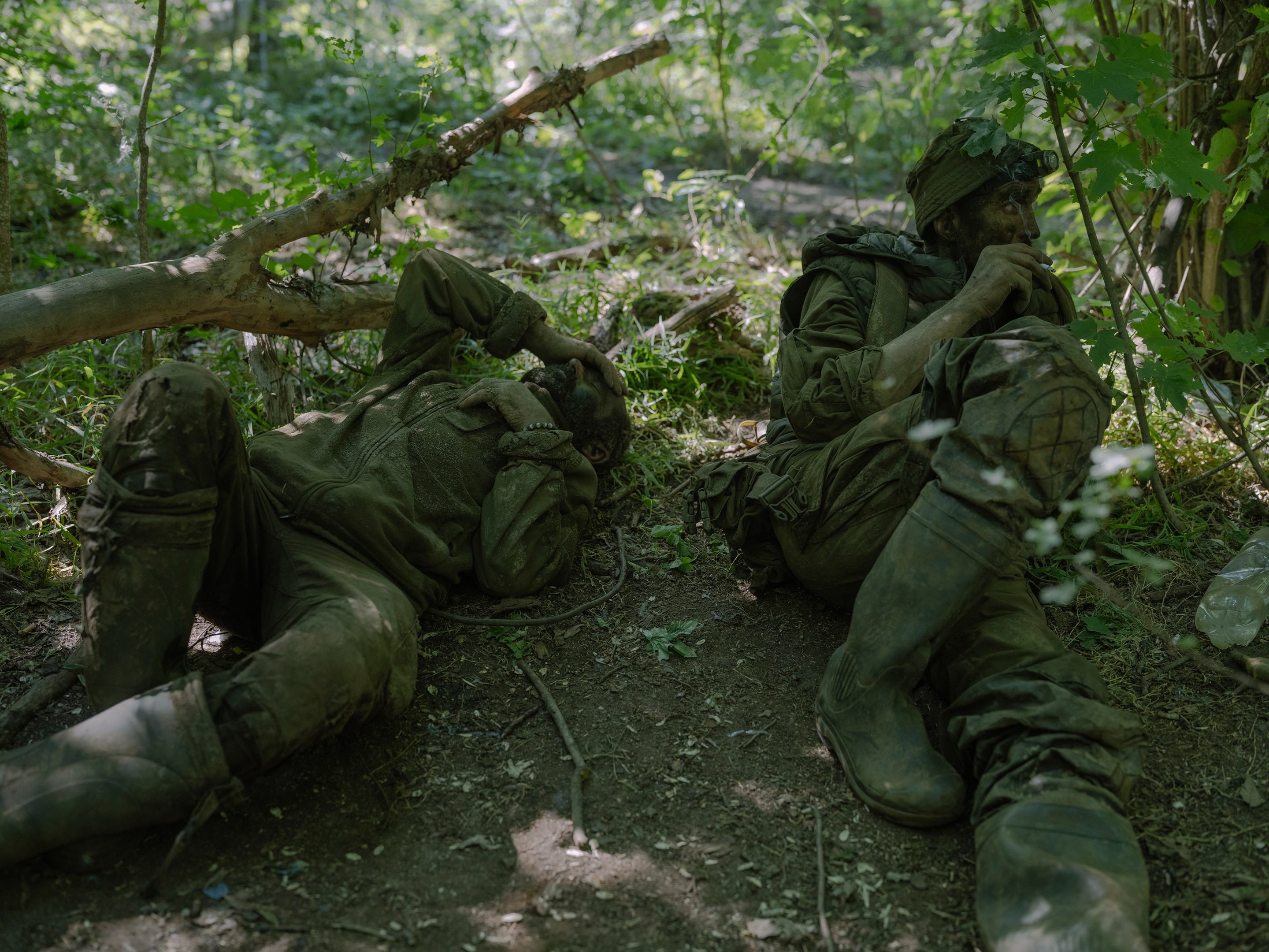 dirty soldiers lay on grass and smoke cigarettes