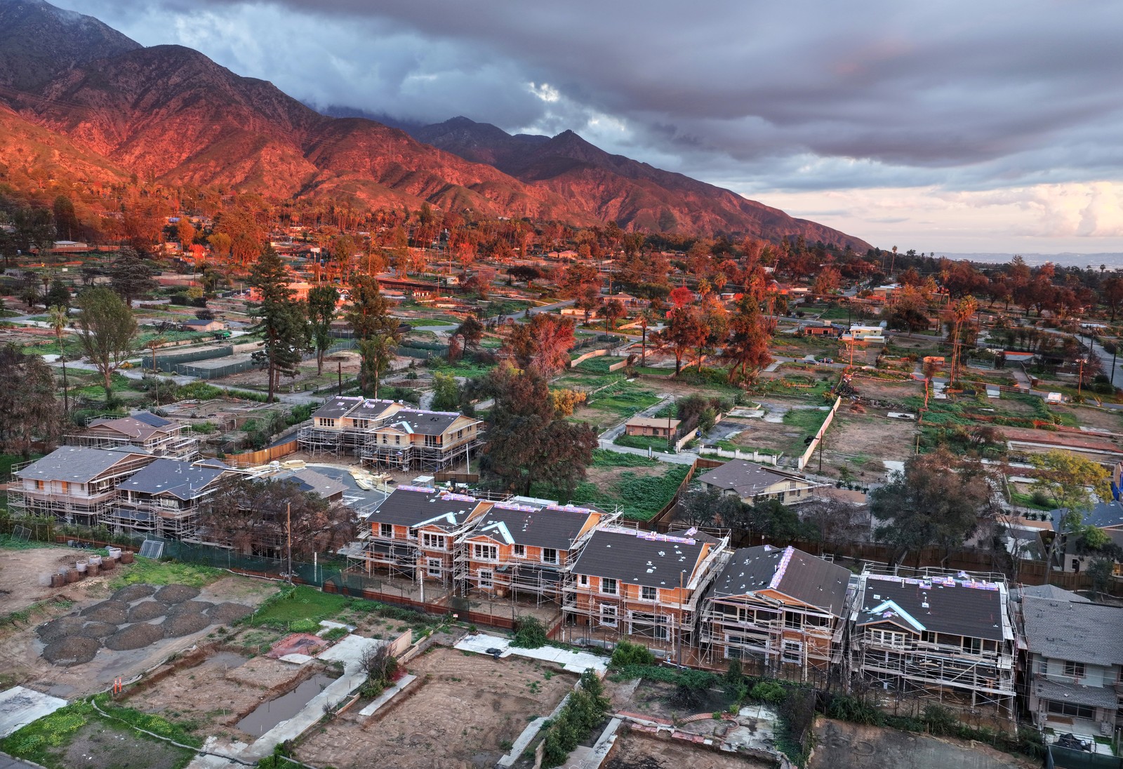 An aerial view of construction of new homes in a hillside neighborhood filled with vacant lots