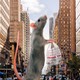 Illustration showing a rat the size of five-story building in New York City standing on its hind legs, carrying a plastic bag