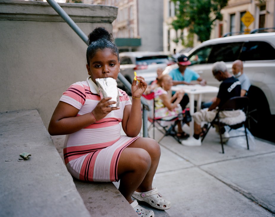 a girl wearing a stripe dress sips a juice on a stoop