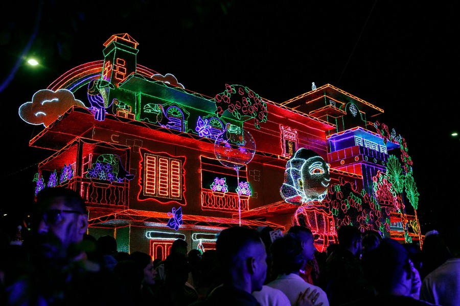 People walk past a large house completely decorated by bright lights.