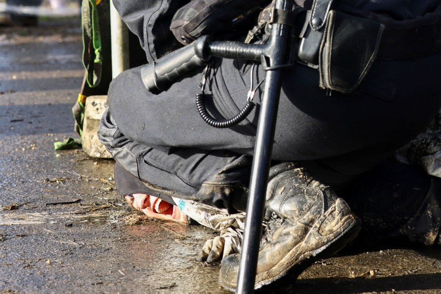 Police officers detain an activist, pressing their face to the ground.