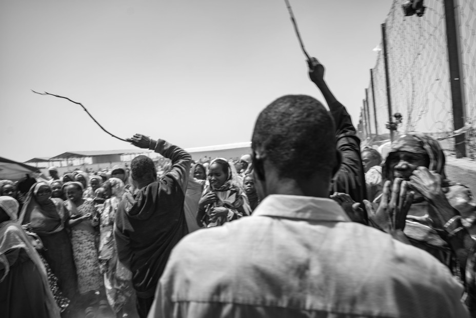 Picture of community members distributing hot meals in Tiné try to fight back Sudanese refugees desperate for food. 