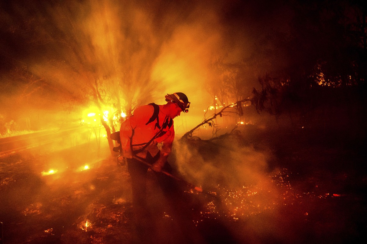 A firefighter works on a forest fire among smoke and embers at night.