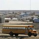 A yellow school bus drives down a dusty road with rolling plains in the background.