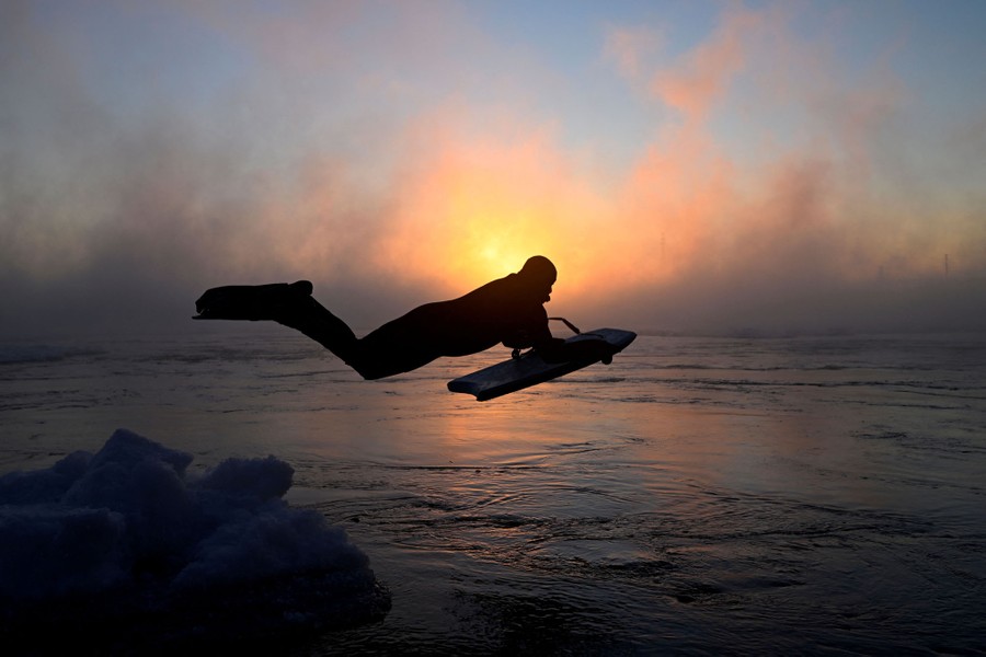 A man leaps into water with a boogie board at sunrise on a very cold day.