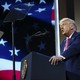 An image of President Trump speaking from a podium in front of a large American flag backdrop