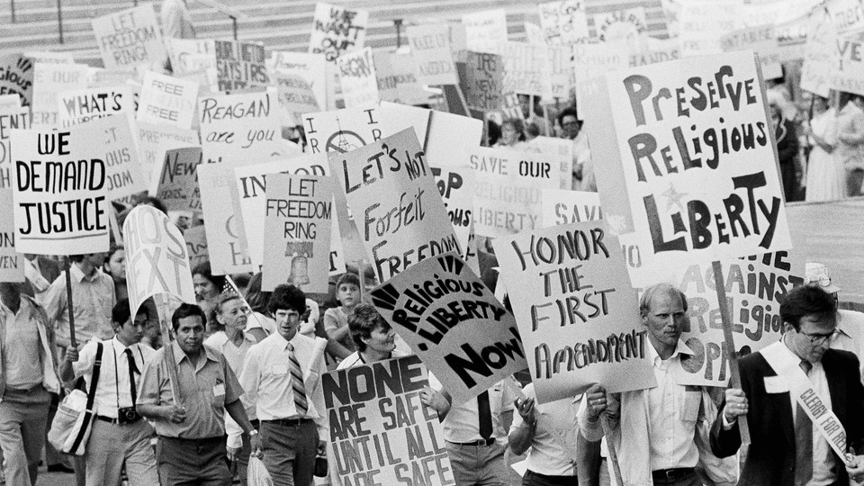 A black-and-white photo of a Reagan-era protest in front of the Supreme Court's steps, with signs reading "Preserve religious liberty" and "Honor the First Amendment"