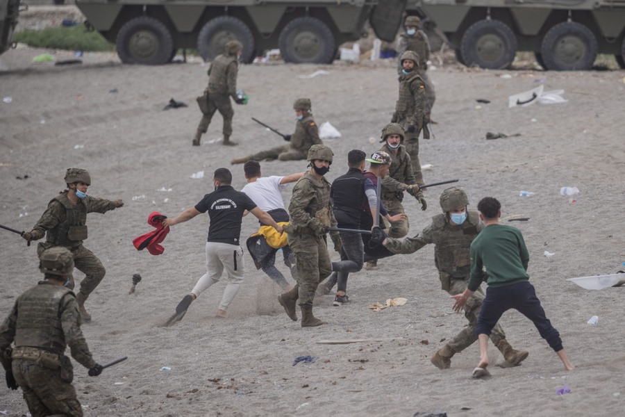 Soldiers swing batons at migrants on a beach.
