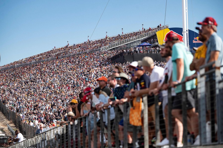 Thousands of fans fill outdoor stadium seats to watch a car race.