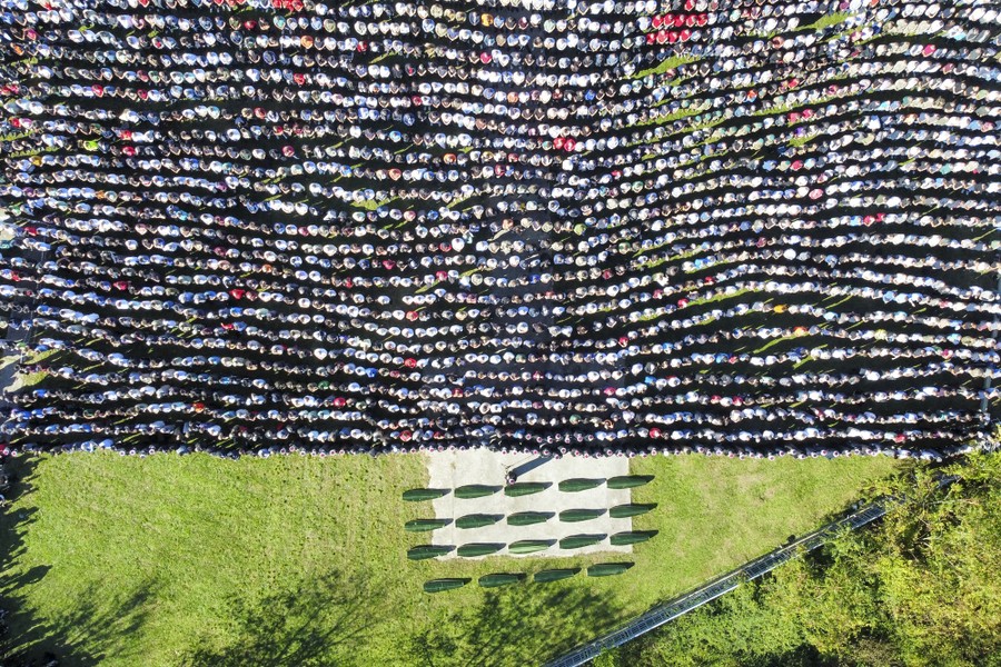 An aerial view of hundreds of mourners standing side by side in rows, at a funeral.