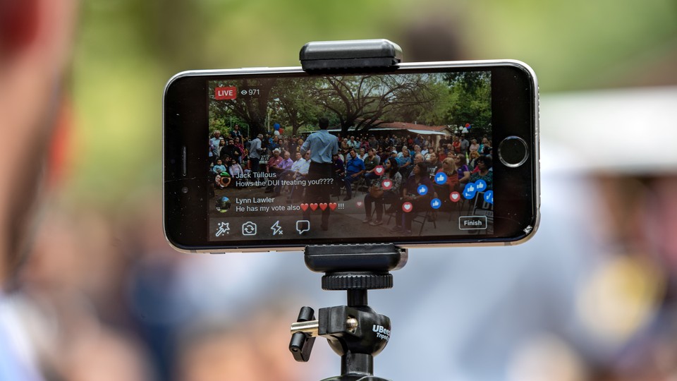 A person uses an iPhone on a tripod to broadcast an event to Facebook Live.