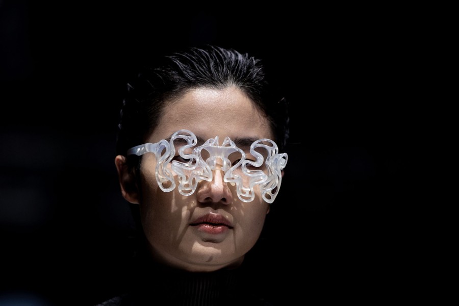 A model displays an ornate pair of glasses, the frame composed of many symmetrical wavy lines.
