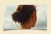 Image of the back of a girl's head as she looks towards the coast