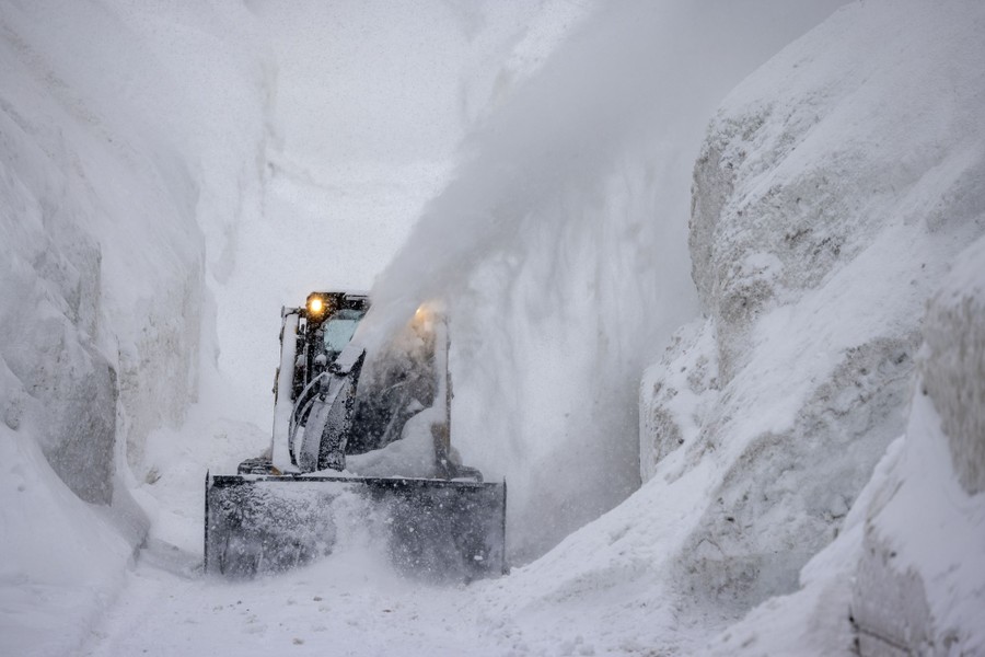 A tractor blows snow from a street that is walled in by very deep snow.