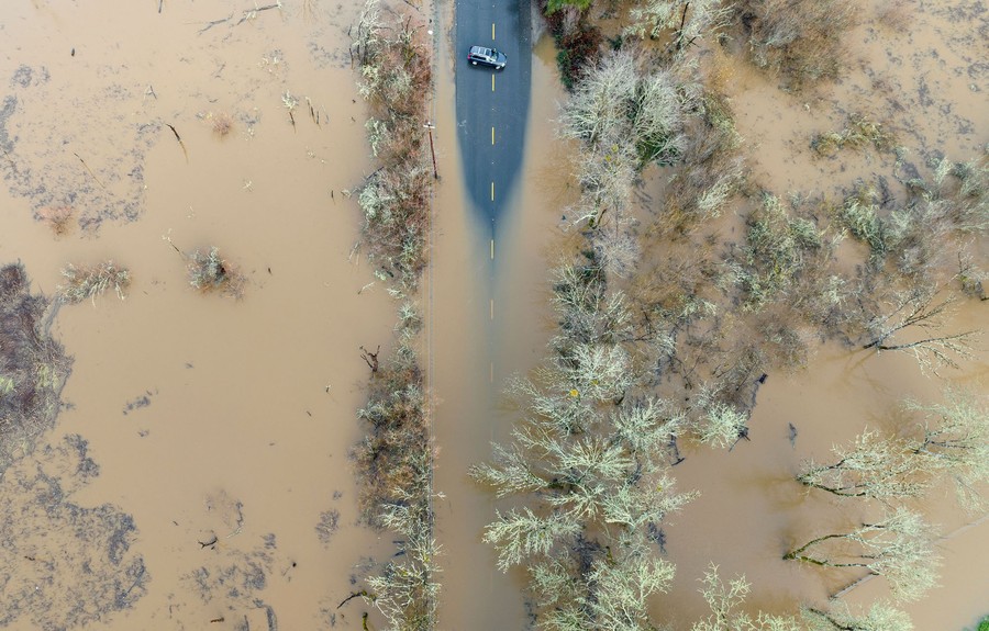An aerial shot of a car sitting sideways on a road that is mostly inundated with floodwater.