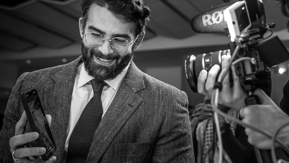 Hasan Piker is photographed smiling and holding his phone screen to the camera.