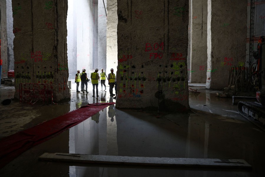 Workers wearing vests and hard hats stand inside a huge underground chamber.
