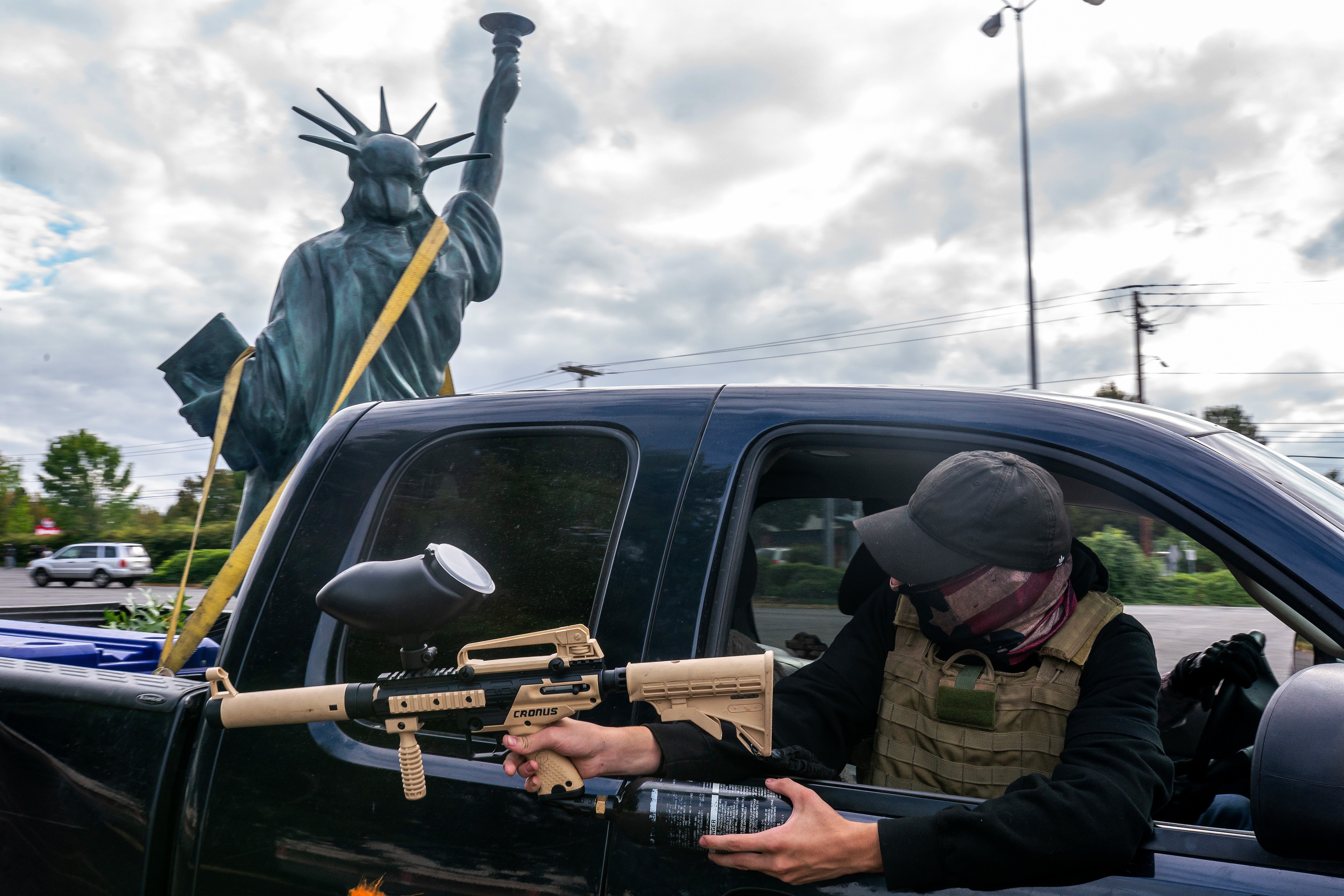 A member of the Proud Boys aims his paintball gun from a vehicle