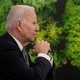President Biden, in profile in front of a wall of green plants, gazes forward with his hands clasped.