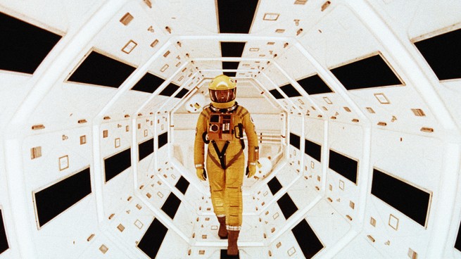Человек в желтом скафандре стоит в футуристическом белом туннеле в сцене из "2001: Космическая одиссея"