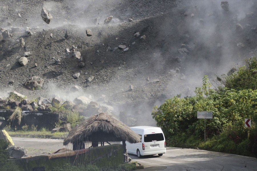 Boulders tumble down a hillside above a white van on a road.