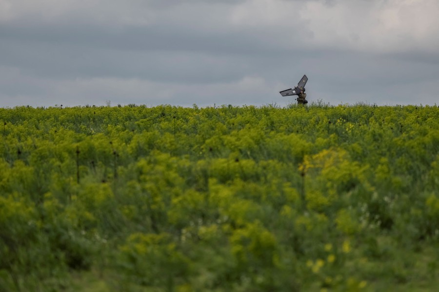 A soldier stands in a wide field, holding a winged drone.