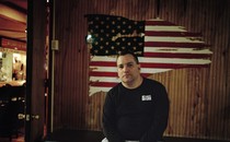 A vet sits in front of a painted flag at a VFW club