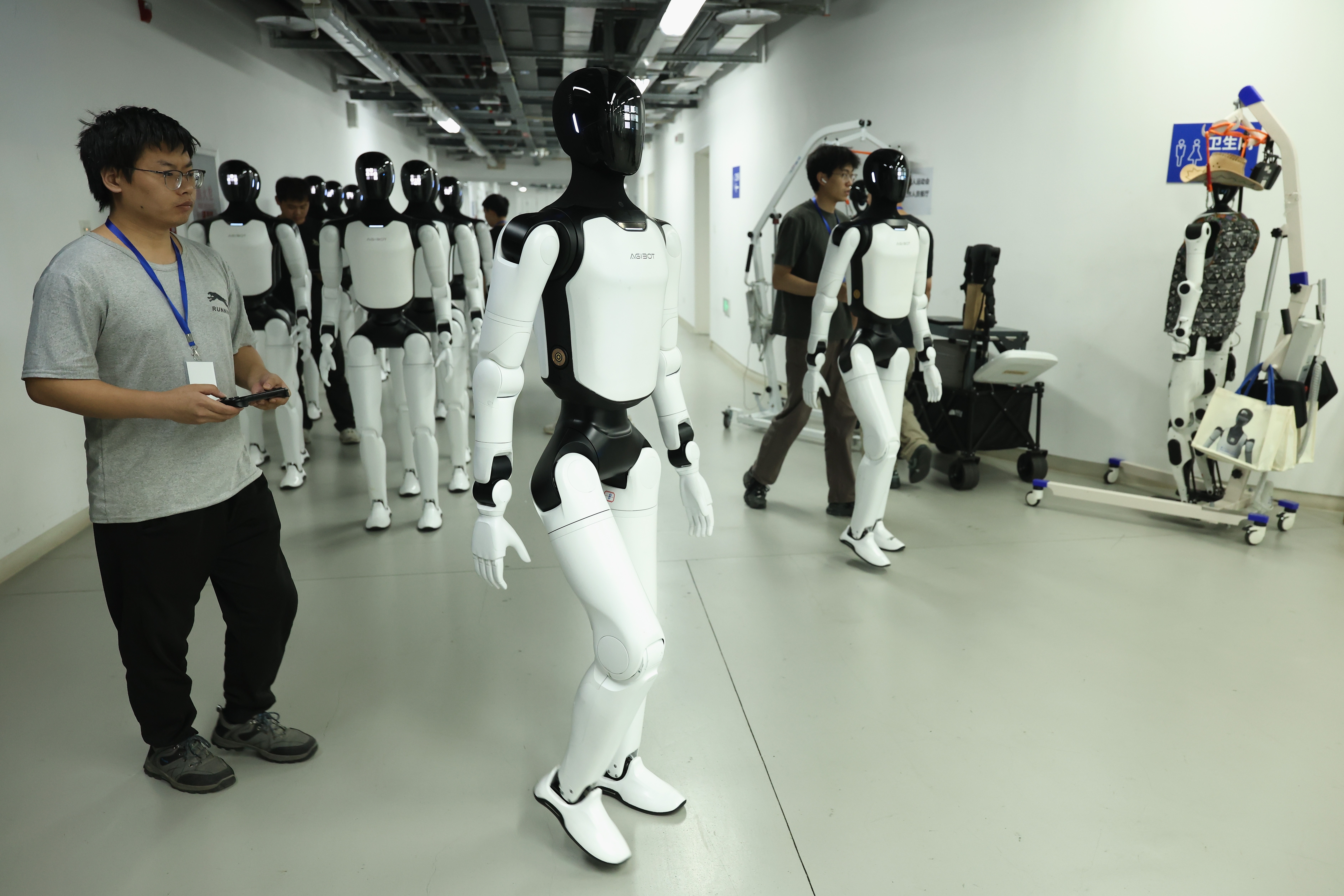 Human technicians guide several humanoid robots in a hallway.