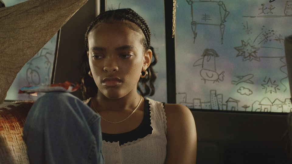 A Black girl with braids sitting inside of a car with doodles on the windows