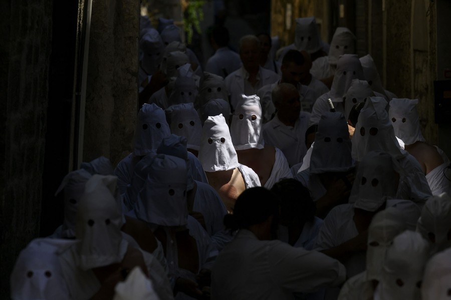 Hooded penitents walk down a narrow lane.