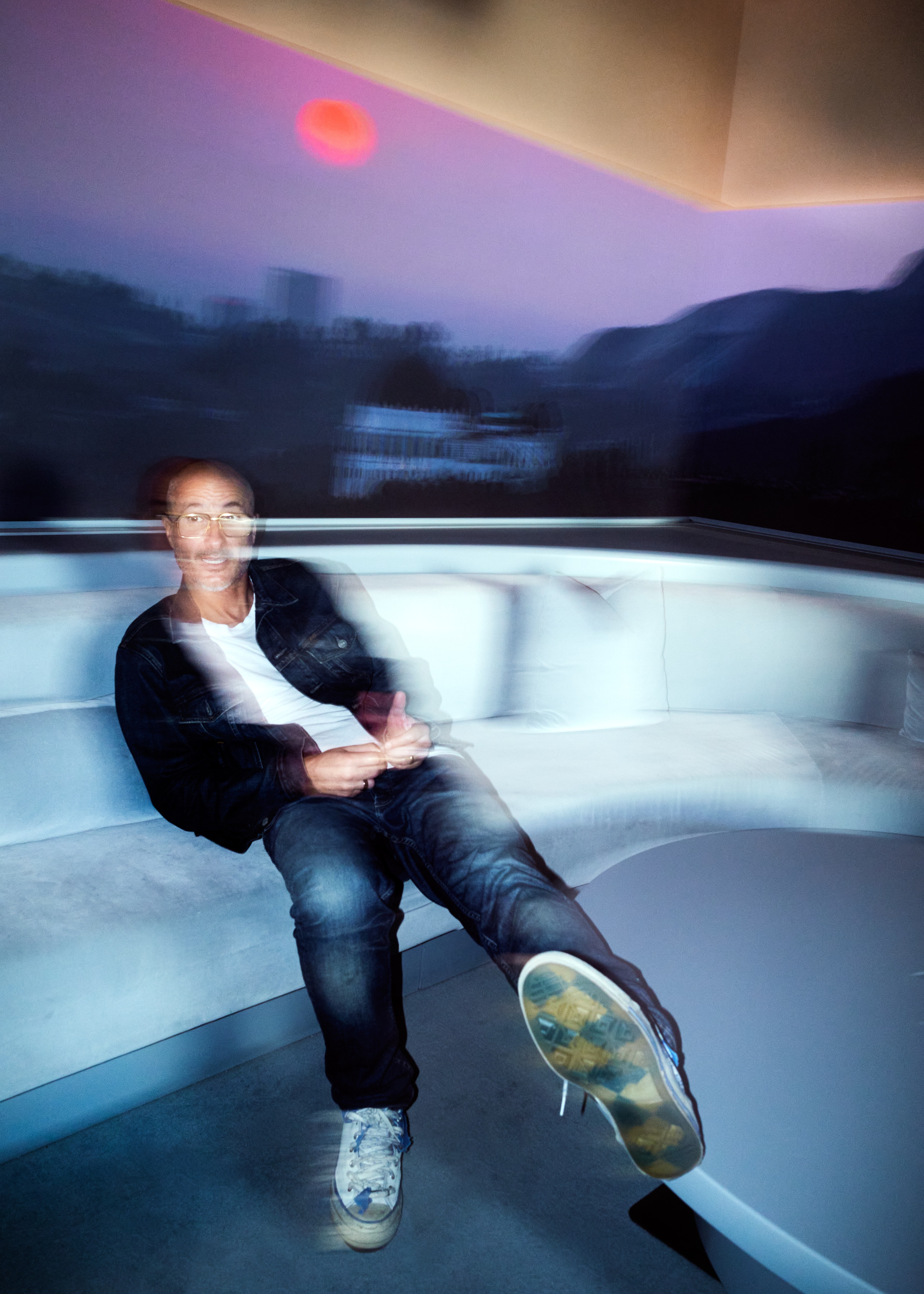 A blurry colorful photo of Zane Lowe sitting on a couch with his feet up on a coffee table
