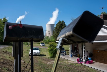 Two black mailboxes in the foreground partially obscure stacks of an industrial facility billowing white steam in the background