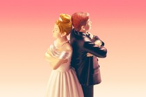 Wedding-cake bride and groom figurines standing back to back with their arms crossed