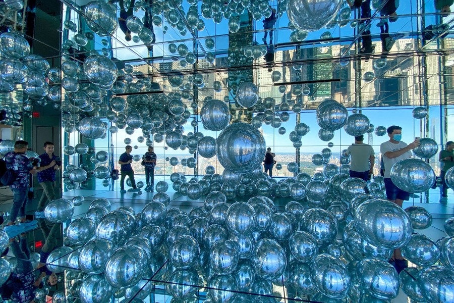 People walk among dozens of mirrored balls arranged around a mirrored room.