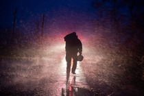 A firefighter walks through strong wind and rain while removing fallen trees at night.