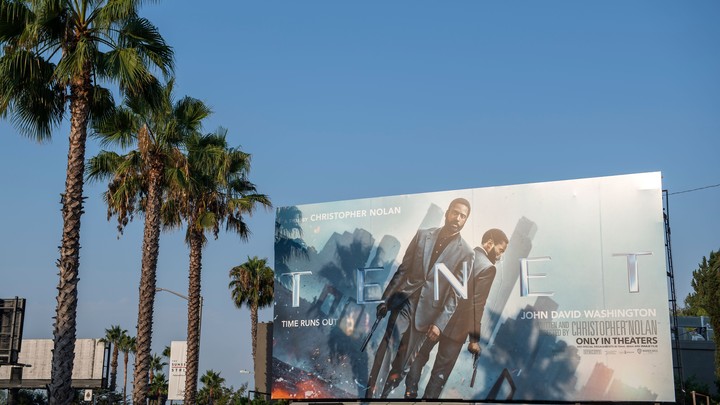 A billboard, showing the actor John David Washington, next to palm trees and against a blue sky