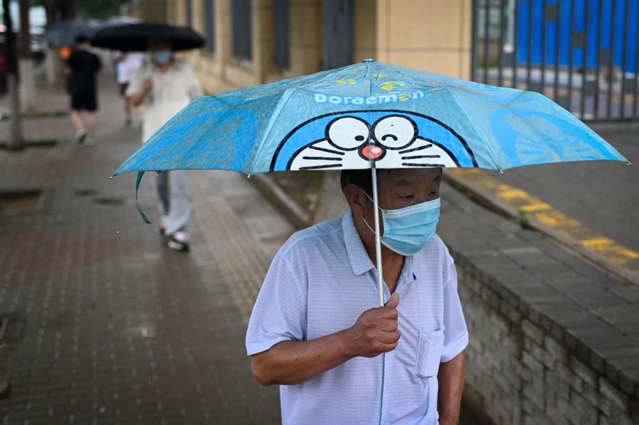 A man on a city sidewalk carries an umbrella featuring the cartoon character Doraemon.