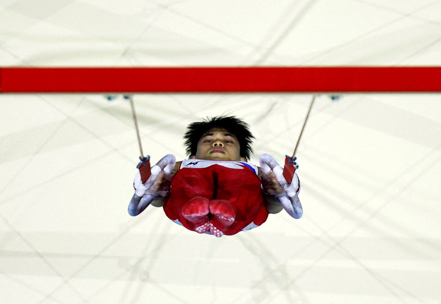 A view looking down at a gymnast who is inverted, hanging from rings