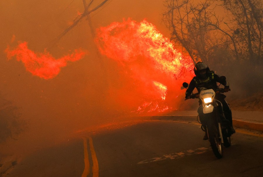 A person rides a motorcycle, fleeing a wildfire.