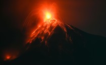 A nighttime view of lava spewing from the top of a volcano and flowing down its slopes.