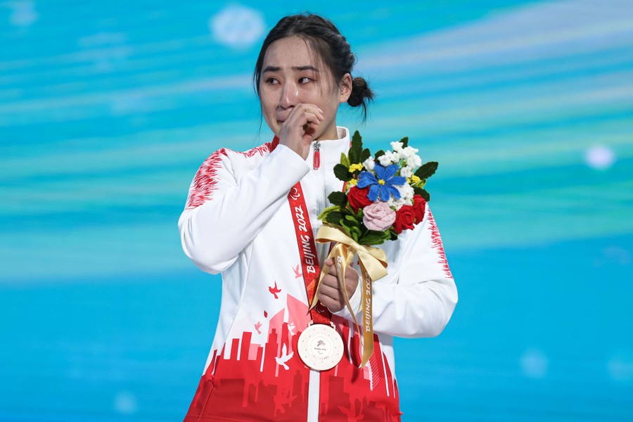 An athlete wipes their face while holding flowers during a medal ceremony.
