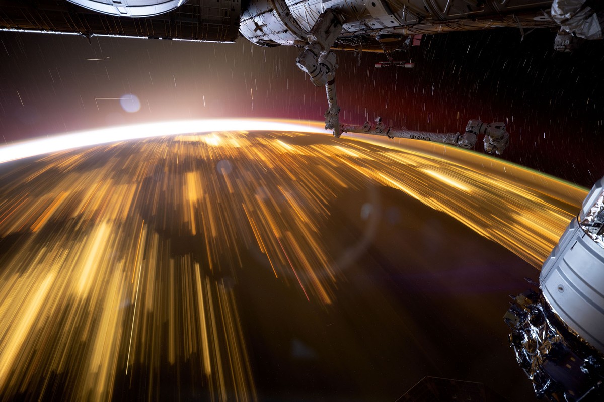 An orbital view of the Earth at night, showing city lights streaking past during a long exposure.