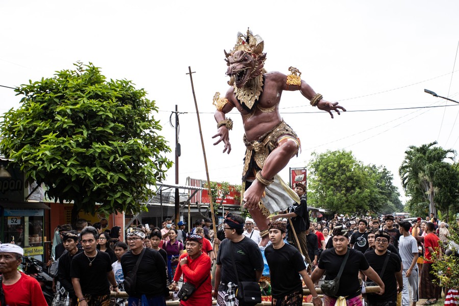 People parade through a street, carrying a tall statue of a frightening demonic figure.