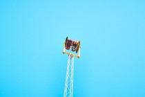 A person sits upside down on an amusement park ride, high in the air.