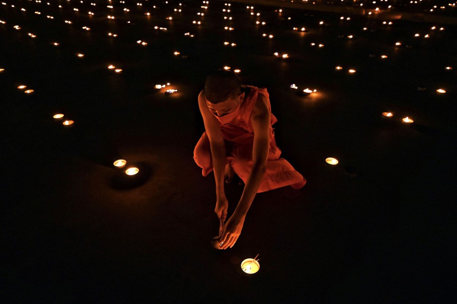 A Buddhist monk lights a candle on the ground, among many others.