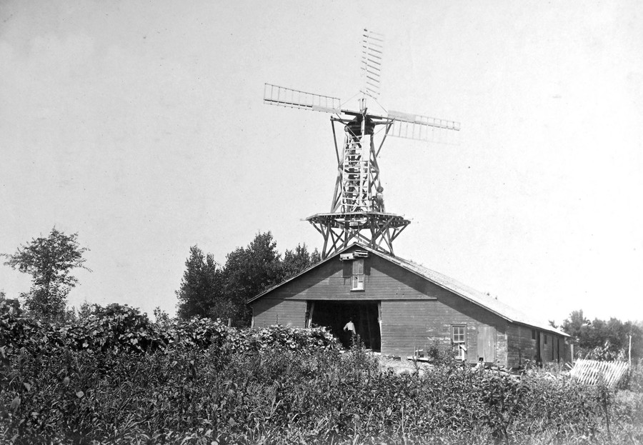 Two children stand on the lower platform of a large windmill that has been built atop a barn.